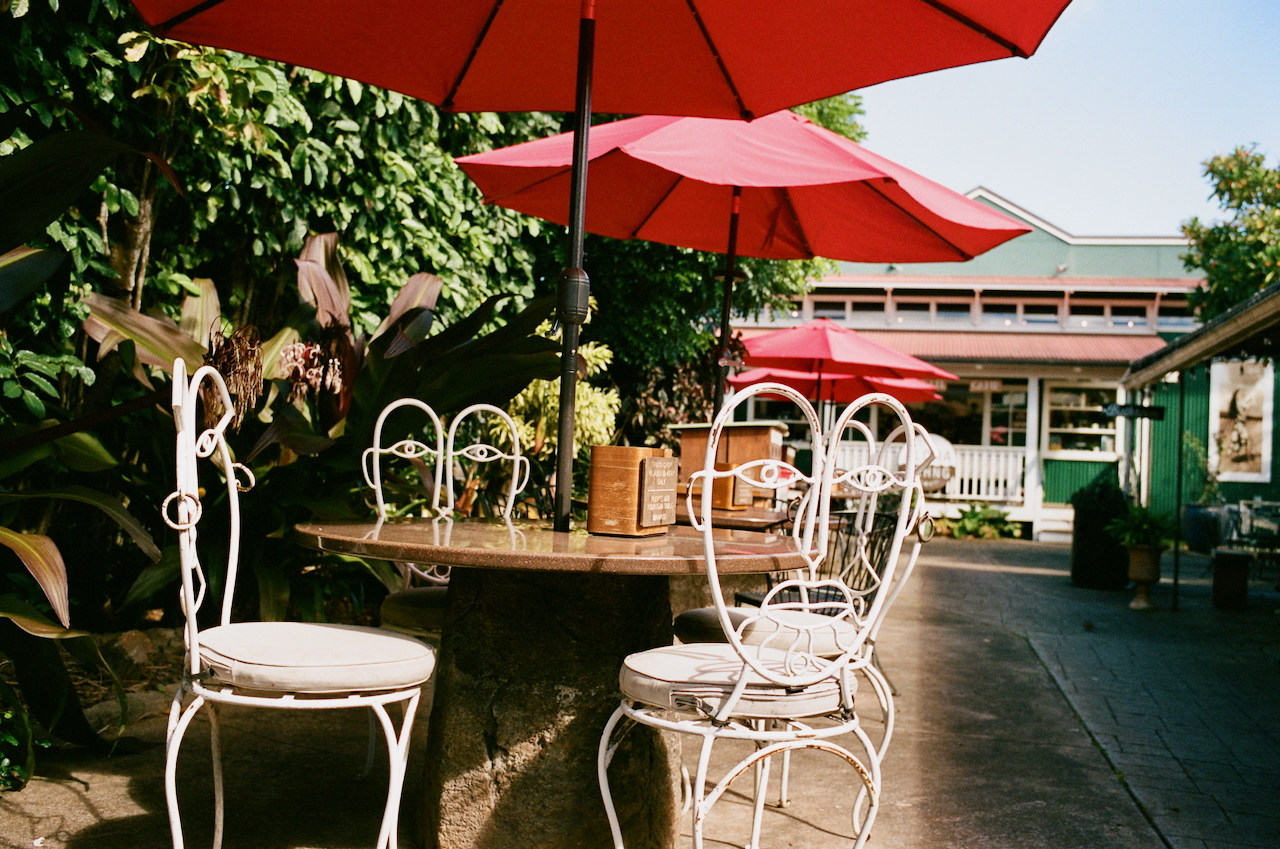 A photograph shows an empty stone table. In the foreground, there are several white wire/metal chairs with faces as the backrest.