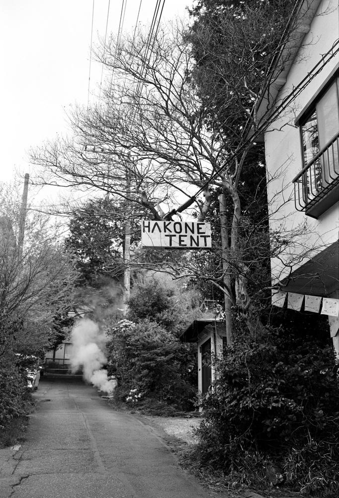 A black and white photo shows a hand painted sign in an alleyway that says Hakone Tent.