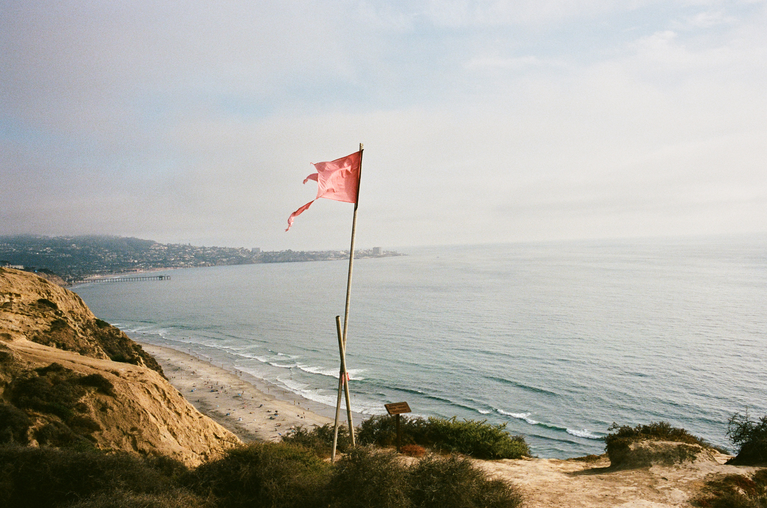 A tattered flag on the cliffside with La Jolla in the background.