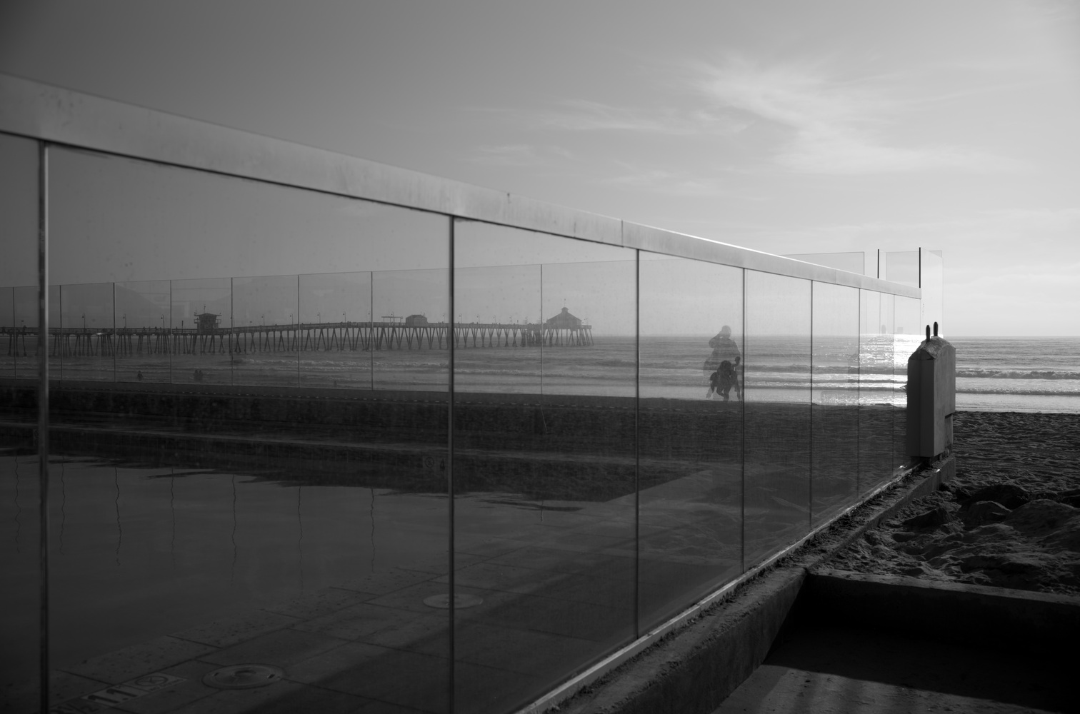 The Imperial Beach pier is viewed through the glass of a pool in the foreground.