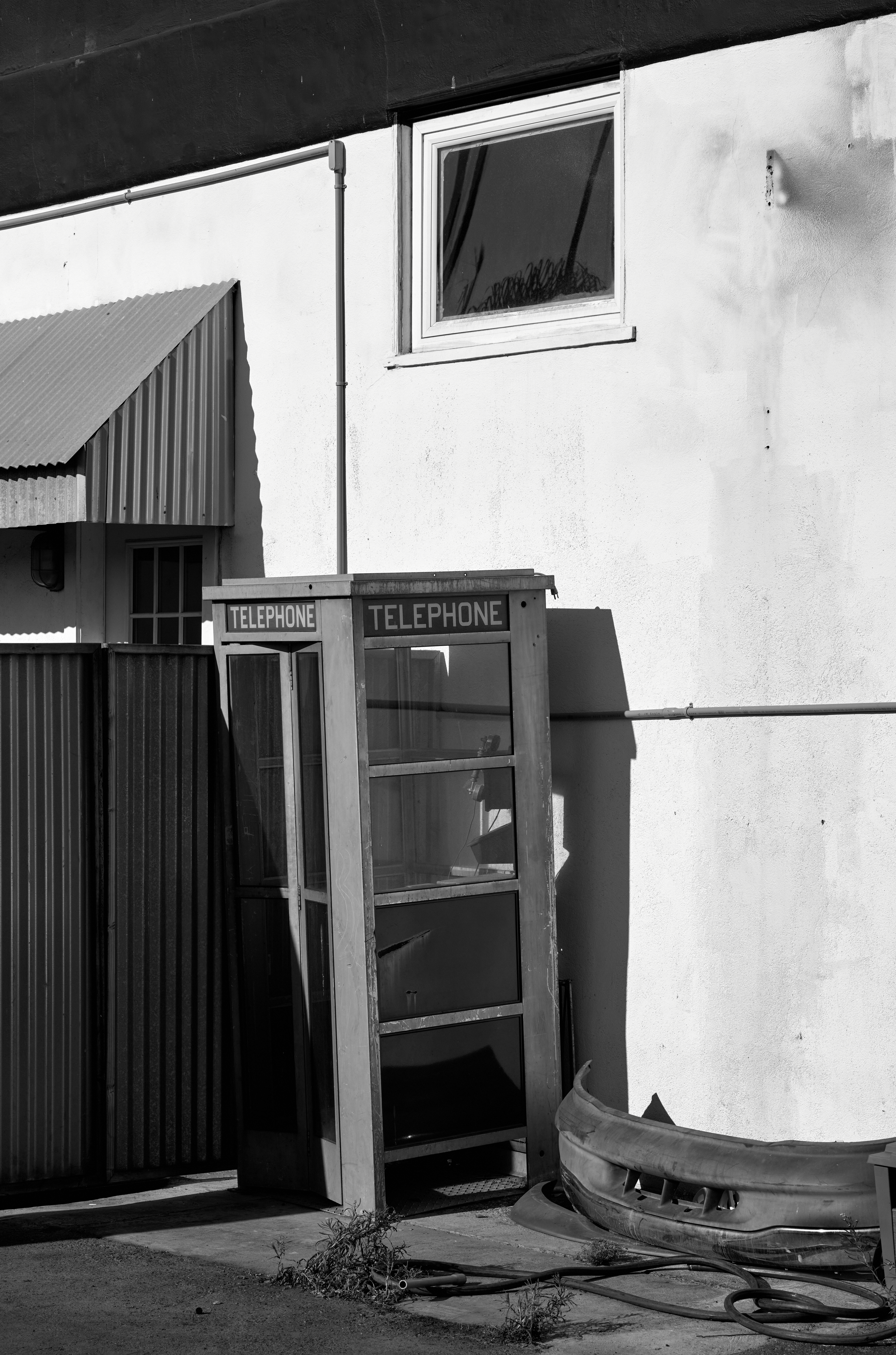A phone booth situated against a building with various other rubbish adorning it.