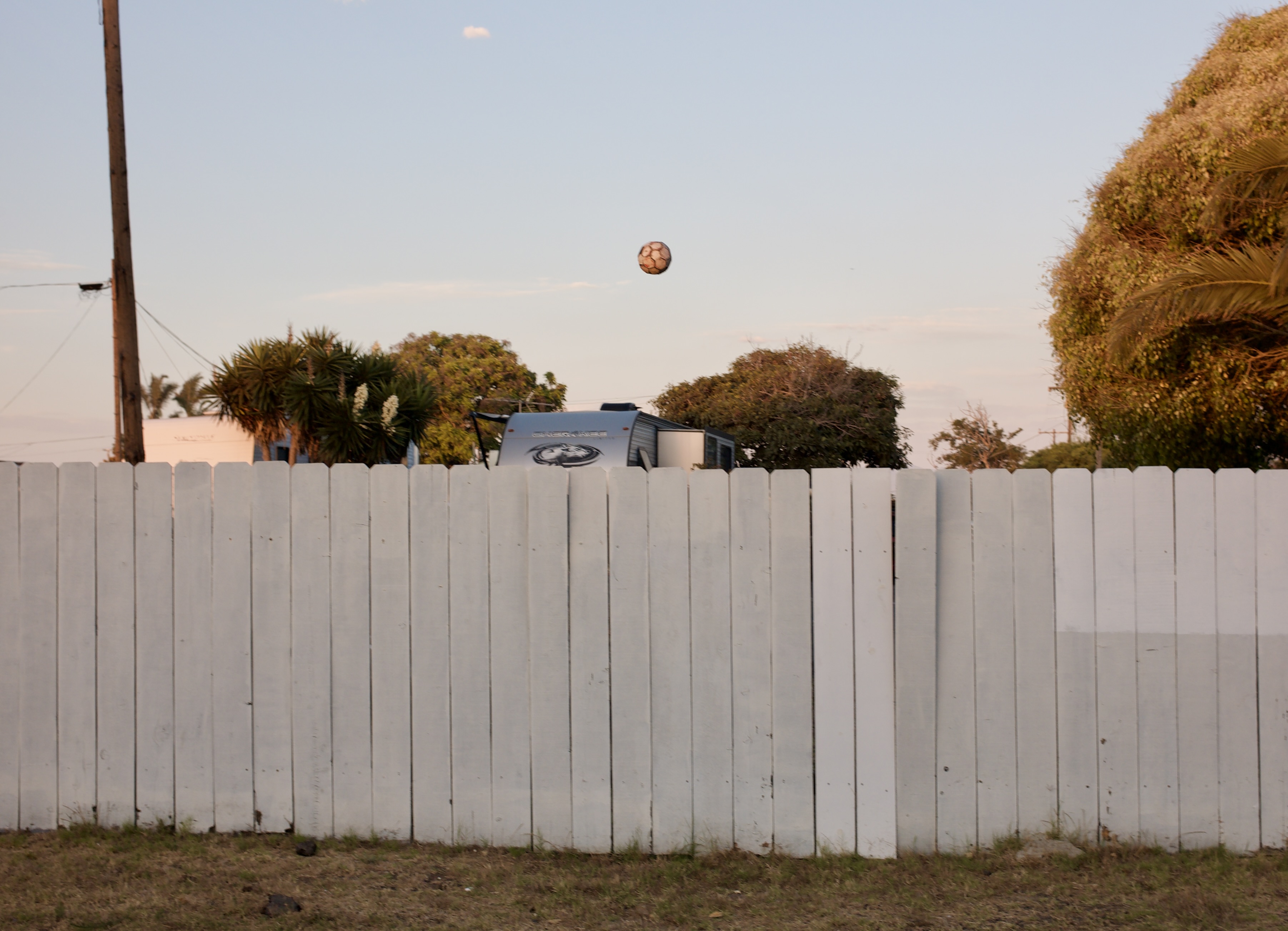 A soccer ball floats mysteriously above a white fence.