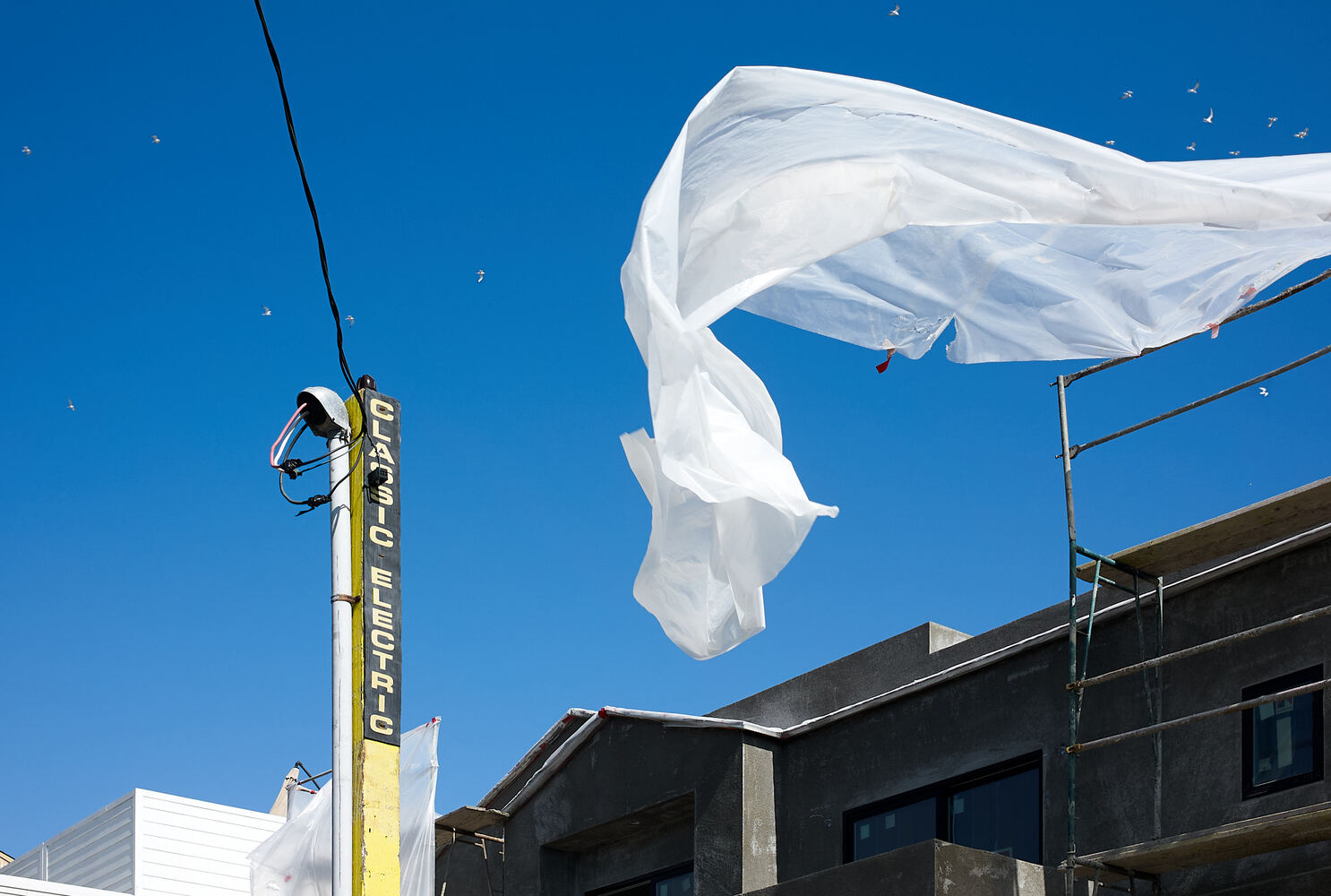A piece of plastic sheathing whips the blue sky.